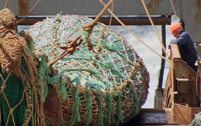A worker aboard a ship observing a large tangled ball or fishing net on deck.